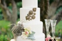 a white wedding cake decorated with neutral and pink blooms, foliage and feathers plus vintage brooches is a chic idea