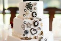 a white wedidng cake decorated with vintage brooches and topped with a bejeweled monogram is a chic and beautiful idea
