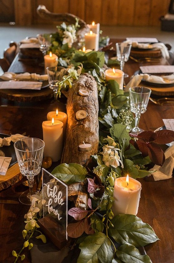 a woodland wedding centerpiece of a tree branch, leaves and foliage, candles and an acrylic sign