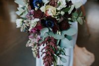 an exquisite cascading wedding bouquet of deep purple, burgundy and neutral blooms and greenery is a gorgeous bold solution for a fall or winter wedding