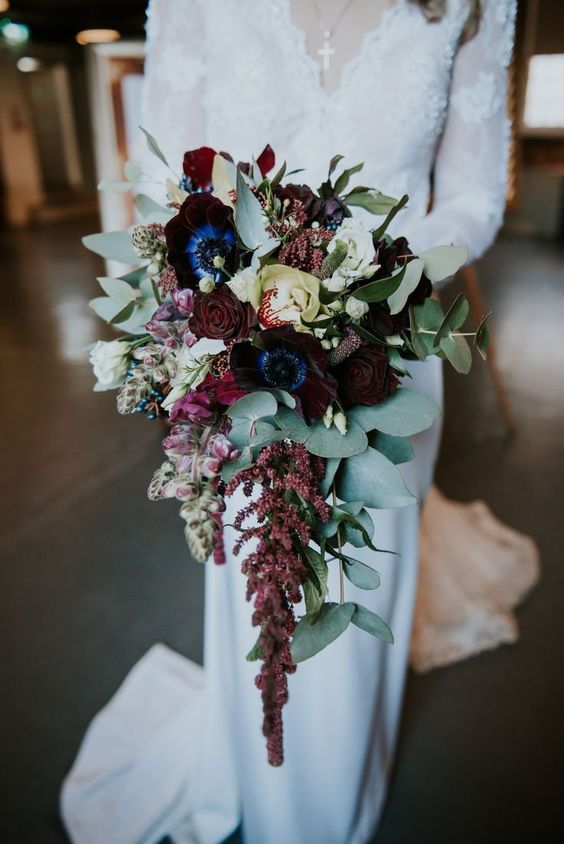 an exquisite cascading wedding bouquet of deep purple, burgundy and neutral blooms and greenery is a gorgeous bold solution for a fall or winter wedding