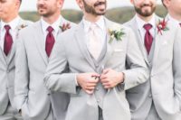 dove grey three-piece suits, burgundy ties and bright boutonnieres for a chic and bold groomsmen’s look