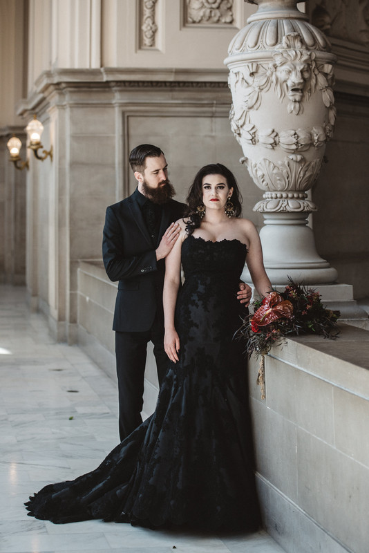 the couple wearing black, the groom in a black suit, shirt and tie, the bride in a black lace strapless wedding dress with a train