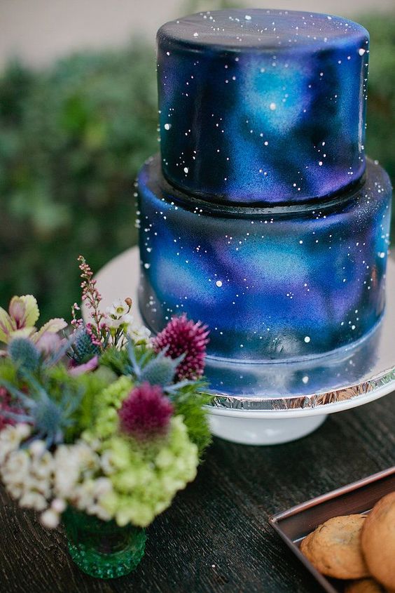 a beautiful blue galaxy wedding cake in black, navy, purple and greenery, with shiny touches that show off stars is a lovely idea for a starry night wedding