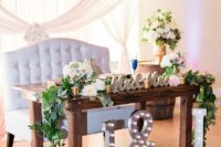 a beautiful rustic wedding sweetheart table with neutral blooms and greenery, a chandelier over it, marquee monograms and an ampersand