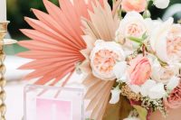 a beautiful wedding centerpiece composed of blush, pink blooms and greenery, neutral and pink paper fans imitating fronds