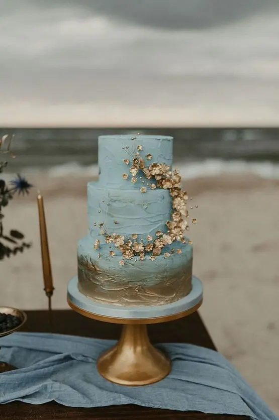 a blue and gold textural wedding cake with gold touches and gold blooms plus beads for decor is a dreamy idea for a beach or coastal wedding