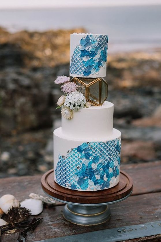 a bold blue wedding cake with a print and brushstrokes, with blooms and a candle lantern in its center