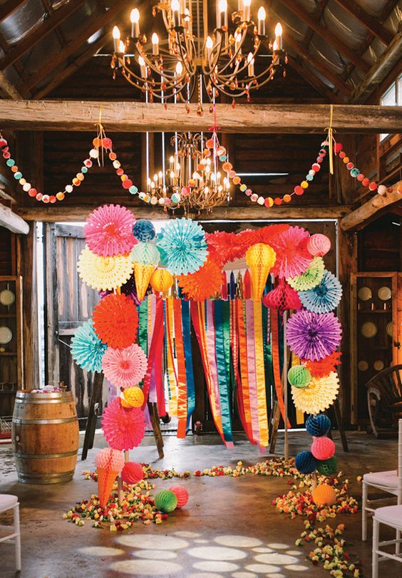 a bright wedding arch decorated with colorful paper fans and ribbons, with bright blooms on the floor