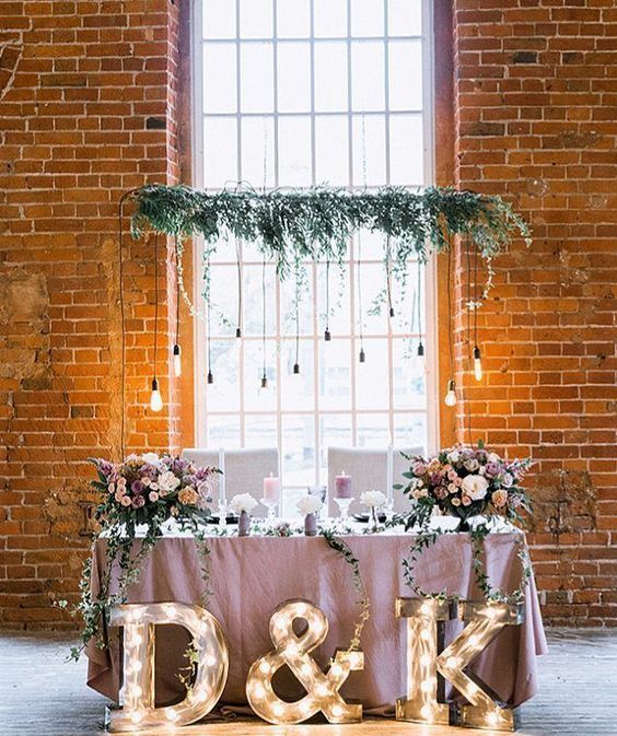 a chic wedding sweetheart table with a lilac tablecloth and lush blooms, greenery and bulbs, marquee letters at the table