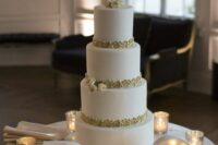a chic white wedding cake decorated with blooms, a gold monogram and gold detailing, small marquee monograms and an ampersand