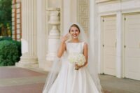 a classic plain wedding ballgown with a pleated skirt, a high neckline and no sleeves, a long train, a cathedral veil