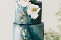 a deep blue marble wedding cake with gold leaf and white sugar blooms is a beautiful and chic idea for a coastal wedding