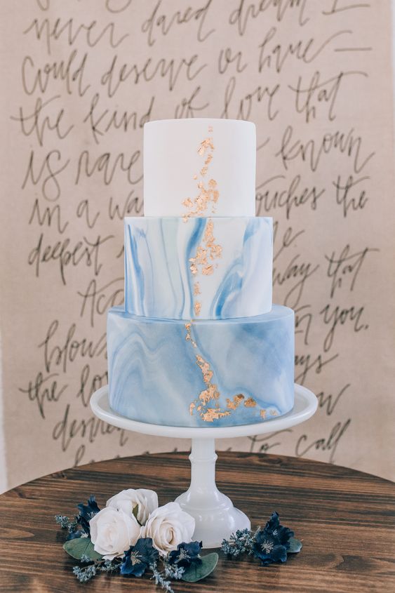 a delicate and subtle wedding cake with white and blue marble tiers, gold leaf is a trendy idea for a modern wedding done with blues