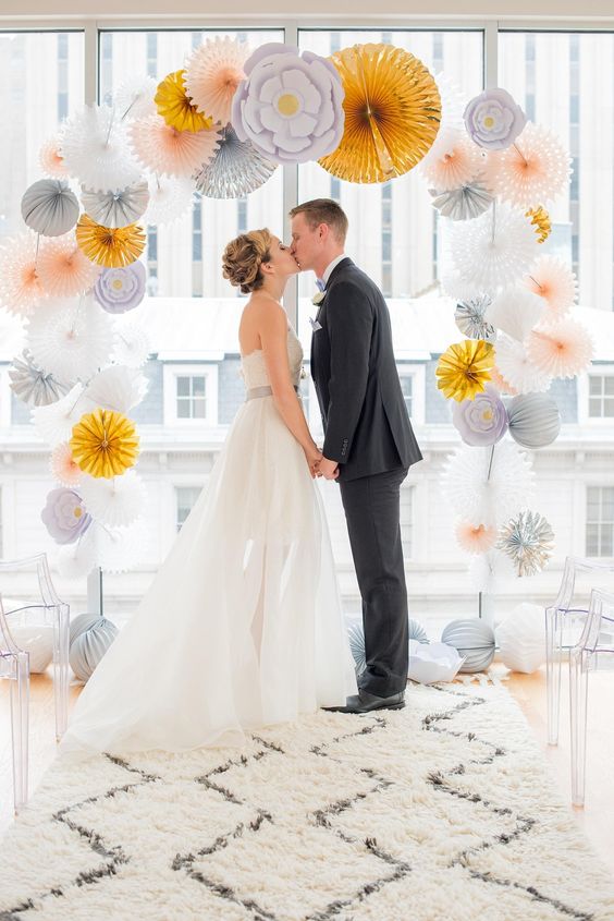 a delicate wedding arch of blush, grey, white and gold paper fans and florals is a lovely idea for a modern wedding