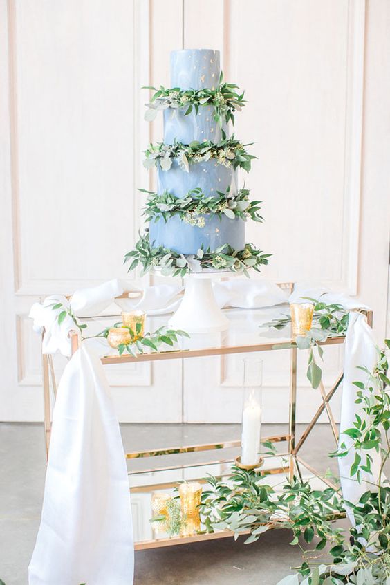 a dusty blue wedding cake with gold leaf and fresh blooms and greenery is a stylish idea for a spring wedding, it looks cool