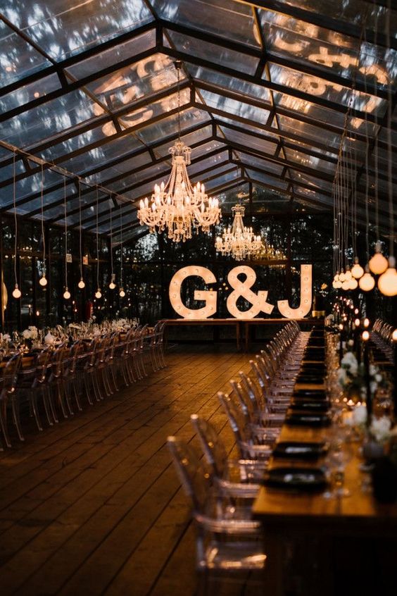 a gorgeous greenhouse wedding venue with chandeliers, bulbs over the table and oversized marquee letters