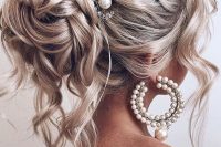 a jaw-dropping wedding hairstyle for long hair, a volume on top, a braided halo, a top knot with waves and curls accented with a pearl hairpiece