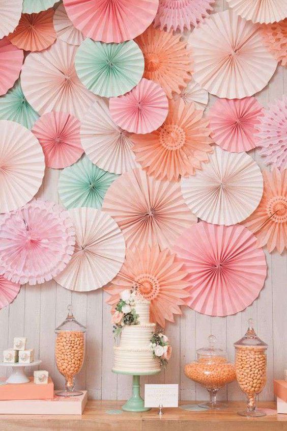 a pastel wedding dessert table and a pastel green and pink plus peachy paper fan wedding backdrop is a lovely idea for a wedding