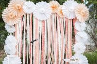 a pretty and simple wedding backdrop with peachy and white paper fans, with pink and white ribbons down is amazing