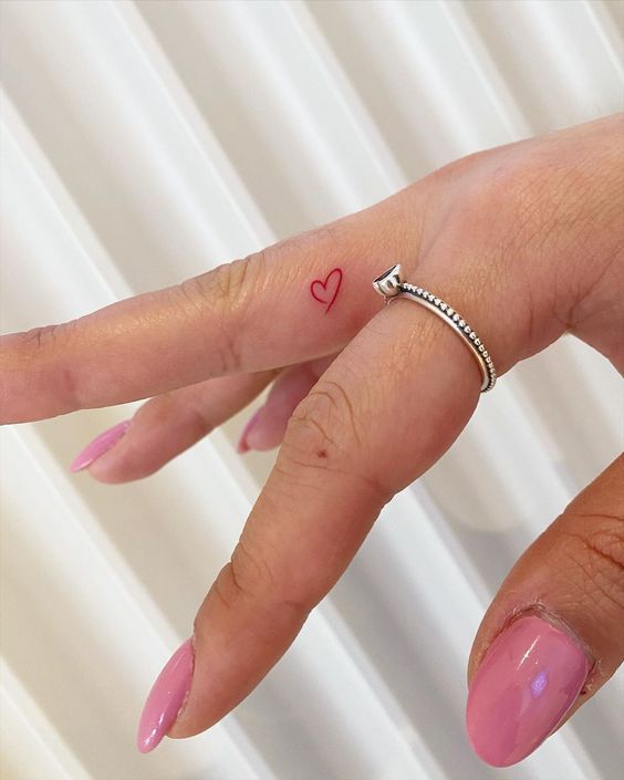 a red heart tattoo on the side of the finger is a cool and cute idea in a bold color but still rather hidden