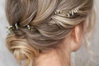a refined and cool wedding updo with a volume on top, a small bun and some locks down plus some blooms tucked into the hair