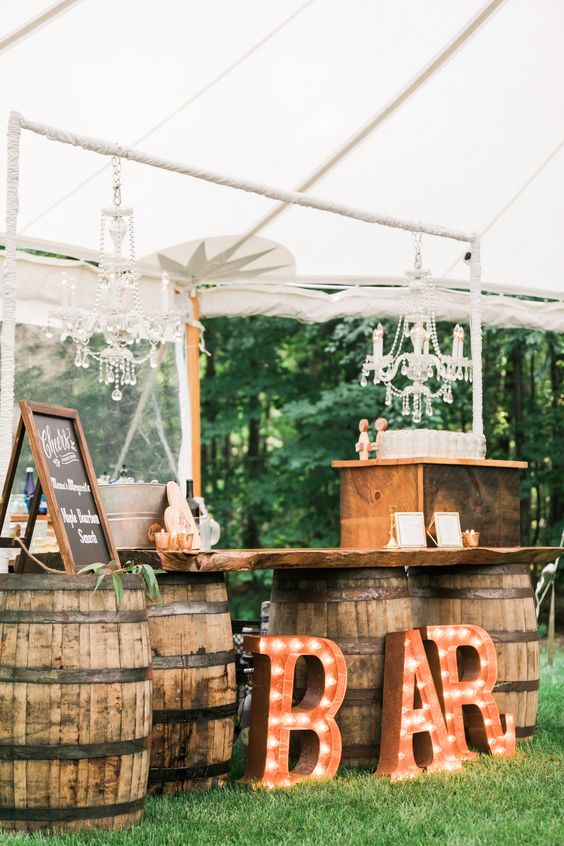 a rustic wedding bar on barrels, with marquee letters, chandeliers and candles is a cool idea for a rustic wedding