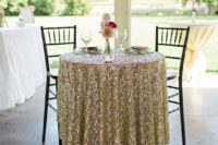 a small couple table with a gold sequin tablecloth, marquee letters and greenery is a lovely and glam decor idea