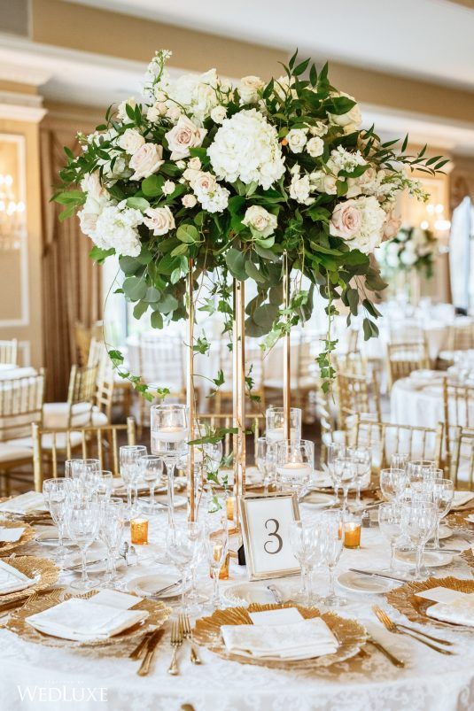 a sophisticated wedding tablescape with gold chargers, cutlery and candleholders, a blush and white centerpiece with greenery
