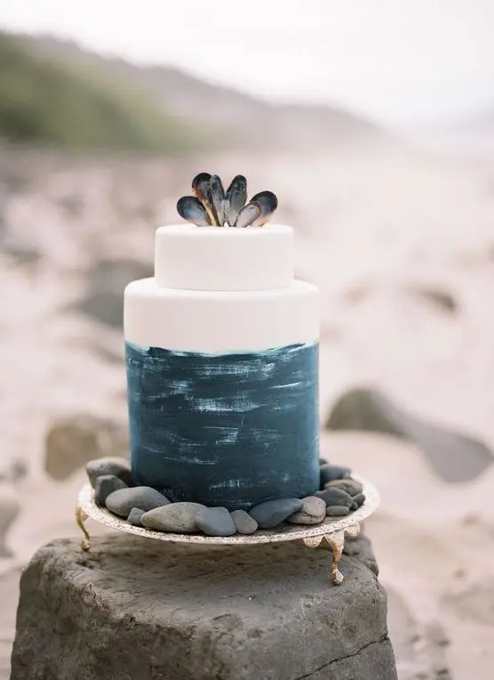 a statement beach wedding cake with navy brushstrokes and mussel shells on top for a beach wedding