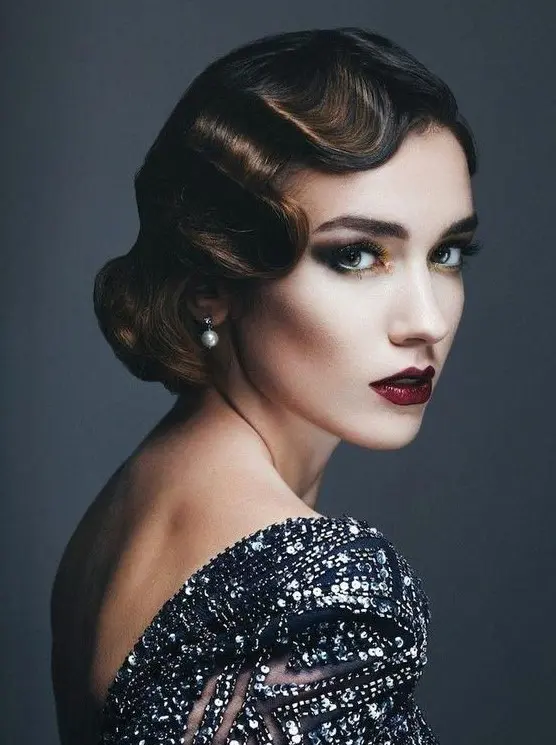 a super chic wavy low updo with color accents and a matching makeup for a modern yet vintage-inspired bride