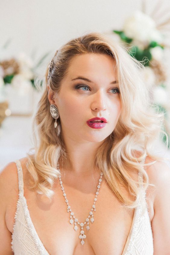 a vintage wavy hairstyle with an embellished hairpiece on one side and a glam makeup with a fuchsia lip
