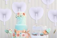a wedding dessert table with white paper fans on the walls and pretty cakes on display is a very cool and stylish idea to rock