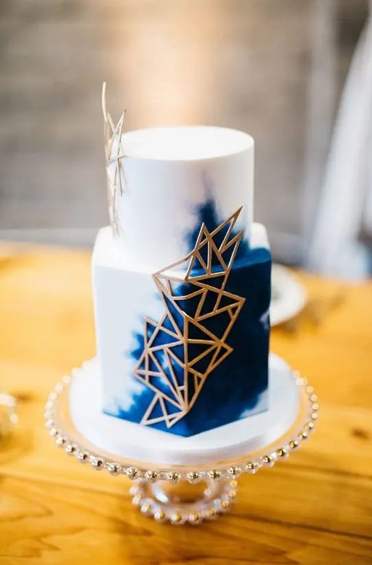 a white and navy watercolor wedding cake with gold geometric detailing for a chic look