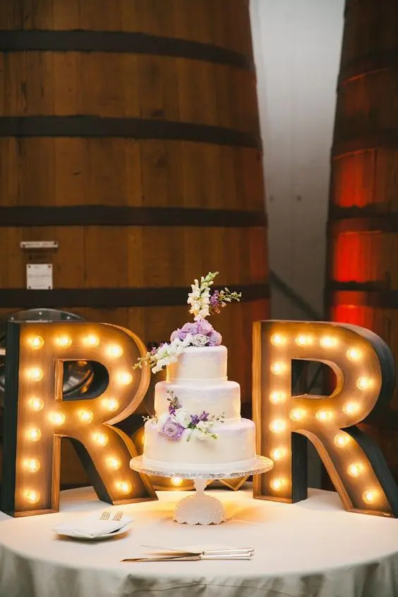 a white wedding cake topped with lilac and neutral blooms, with R letters that accent it is a very cool and bold idea