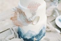 a white wedding cake with blue watercolors, corals and a seashell with pearls for a beach wedding