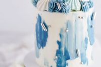 a wihte wedding cake with light and bold blue brushstrokes, silver beads and lots of blue, mint and white meringues on top is amazing