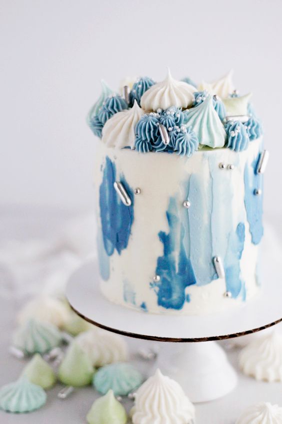 a wihte wedding cake with light and bold blue brushstrokes, silver beads and lots of blue, mint and white meringues on top is amazing