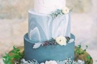 an adorable wedding cake with a plain blue, blue marble and white marble tier, white blooms and pale leaves