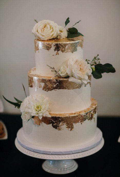 an elegant white and gold leaf wedding cake with white and blush blooms and greenery
