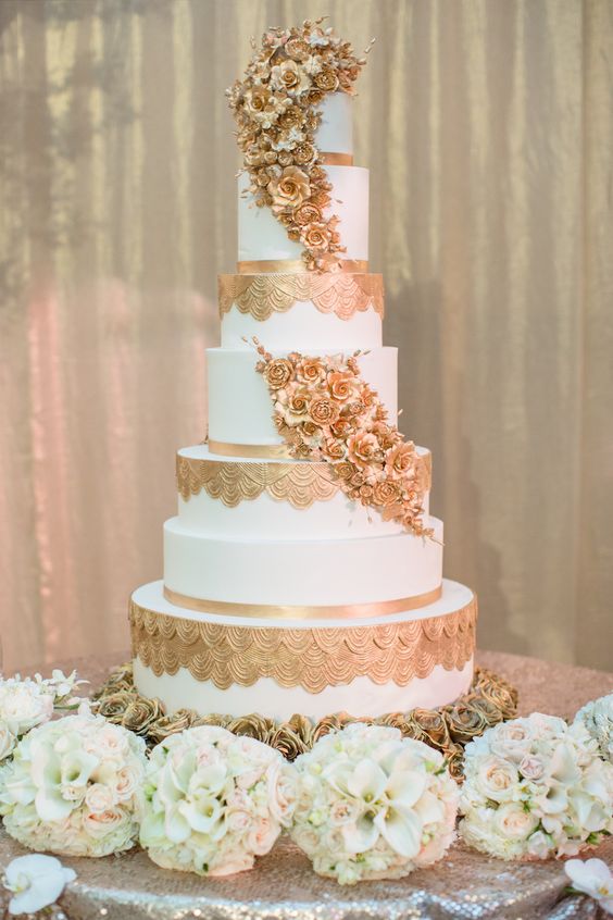 an exquisite white and gold wedding cake with patterns, sugar gold blooms covering the whole cake