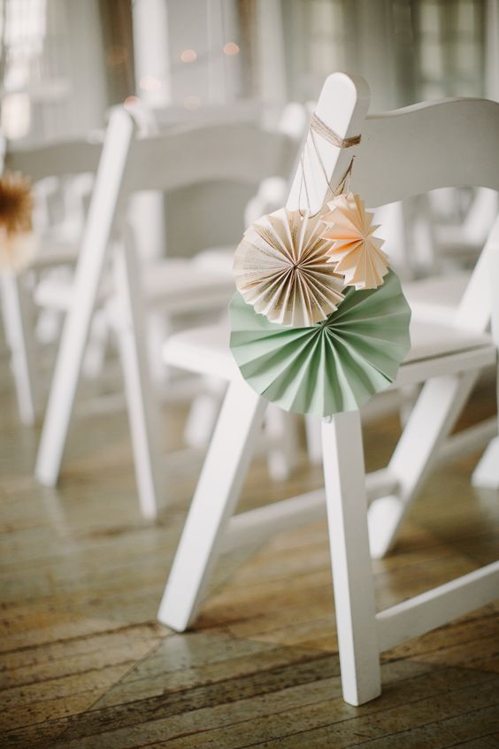 decorate wedding chairs with simple pastel paper fans - that's cheaper than blooms and easy