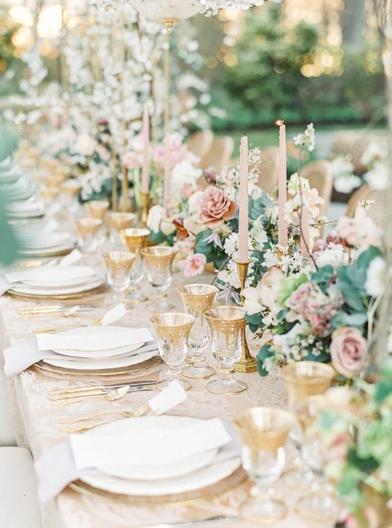 a beautiful blooming wedding tablescape with neutral and pink blooms, blush candles, gold-rimmed glasses and plates