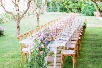 a beautiful outdoor spring wedding reception with pink blooms hanging on the trees, a lush table runner of bright blooms and greenery