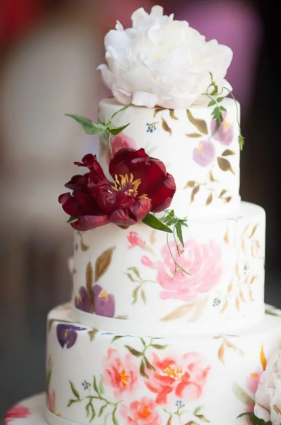 a beautiful secret garden wedding cake with painted pastel blooms and leaves and some bold fresh flowers is wow