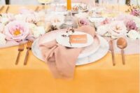 a beautiful spring wedding table setting with a yellow tablecloth and a candle, pink and blush blooms and a pink napkin