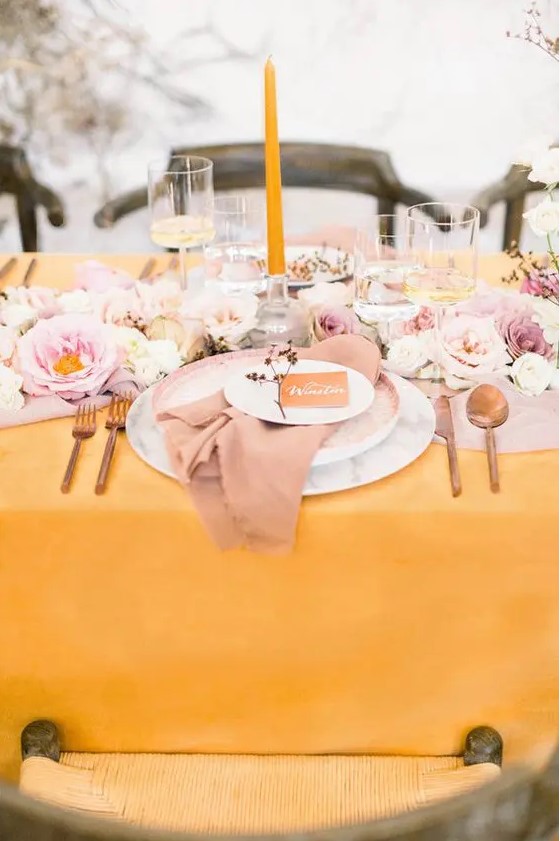 a beautiful spring wedding table setting with a yellow tablecloth and a candle, pink and blush blooms and a pink napkin