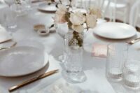 a beautiful spring wedding table setting with neutral and blush blooms, white linens and gold cutlery, elegant glasses is chic