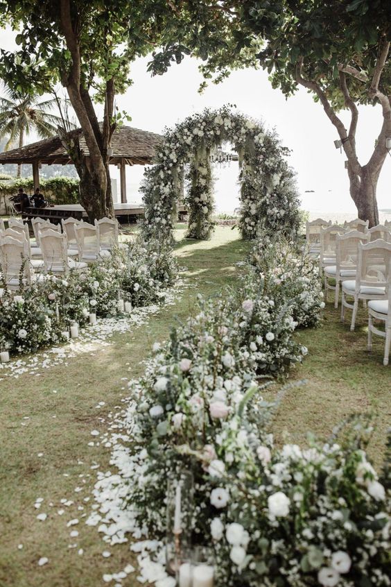 a beautiful wedding ceremony space with a lush greenery and white wedding arch and matching aisle decor is amazing