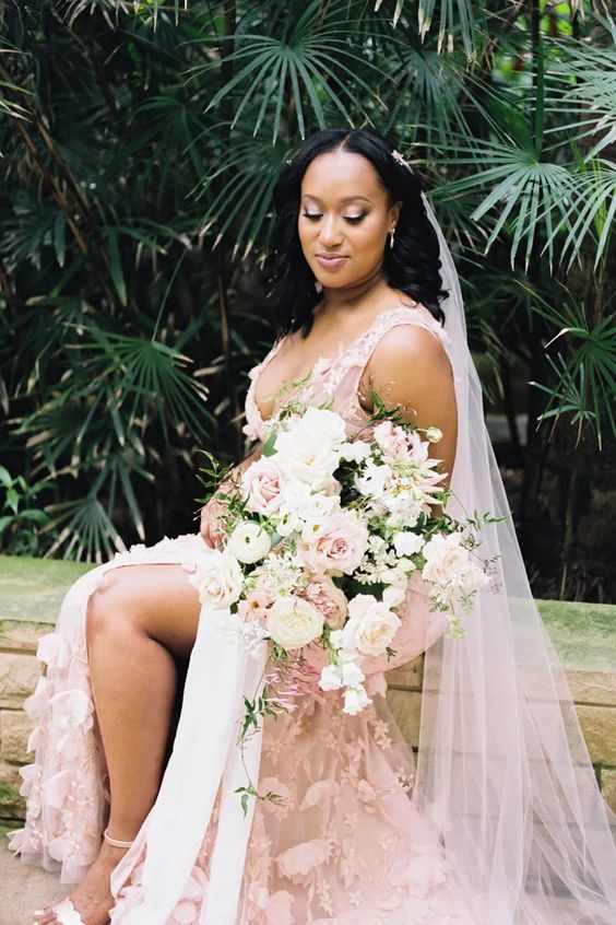 a blush A-line wedding dress with floral appliques, a slit and a deep neckline plus a matching blush veil for a romantic bride